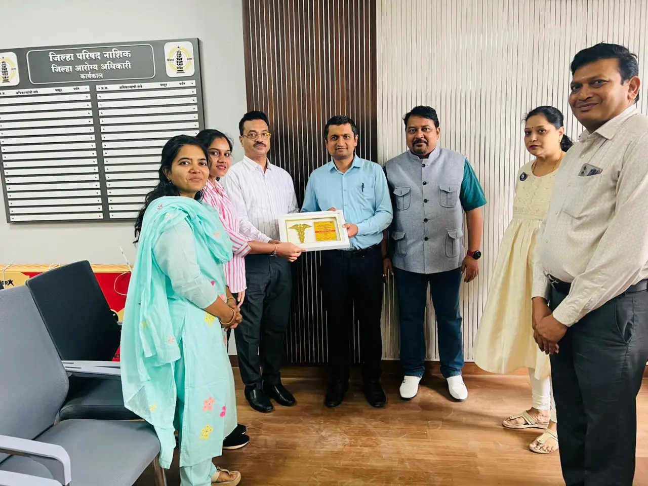 A framed “Token of Gratitude” plaque is presented to one of a group of people standing in an office with a Marathi name board on the wall