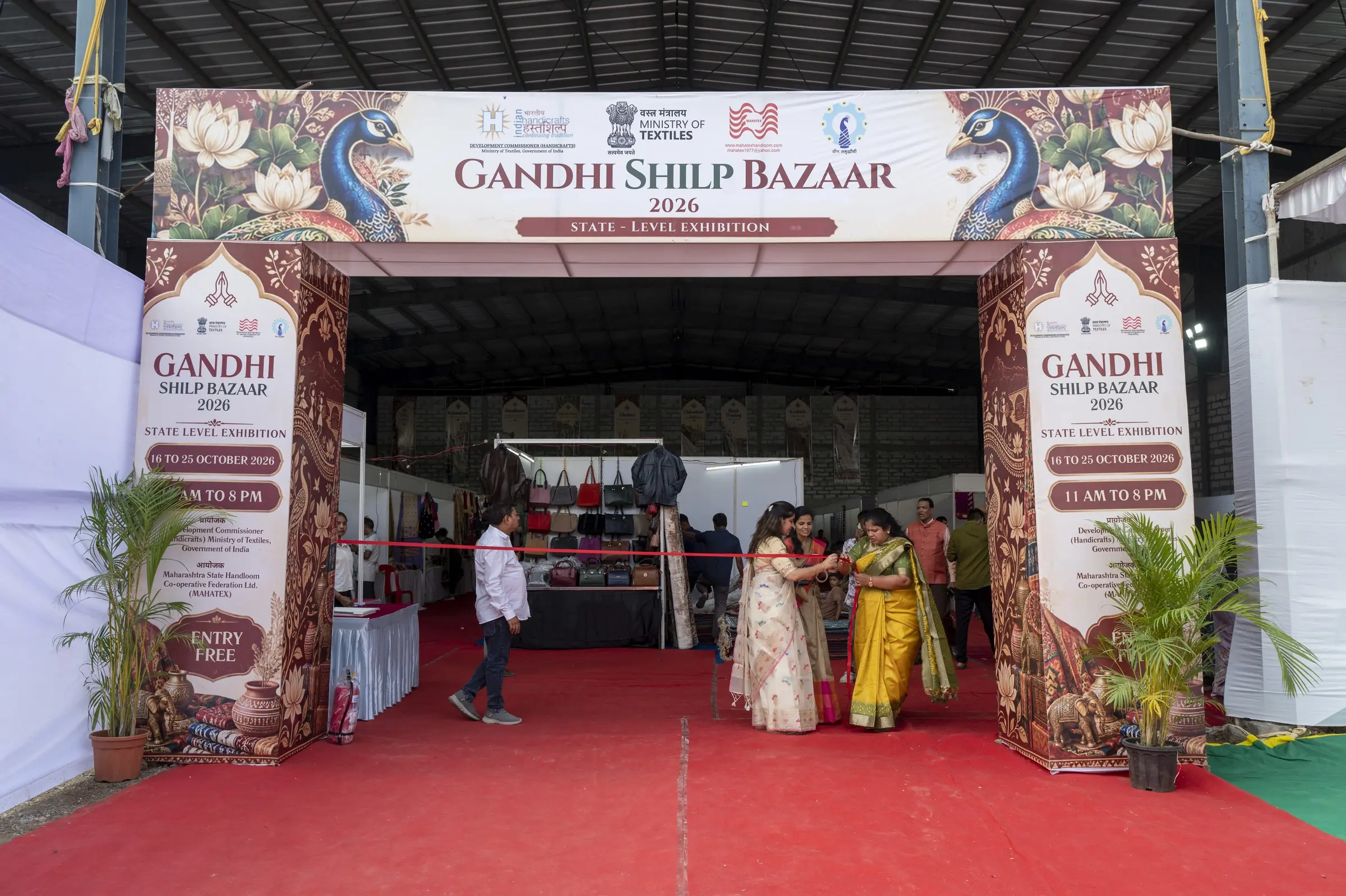 The entrance arch of Gandhi Shilp Bazaar, with the state level exhibition banner, two tall pillars printed with the dates and a red ribbon across the way in