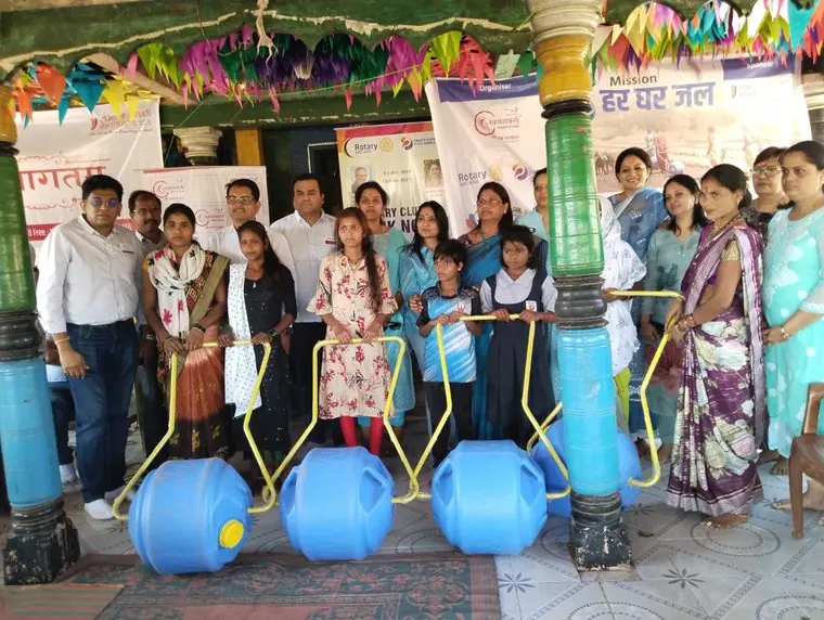 Participants and young people holding Well on Wheel water carriers in front of a Mission Har Ghar Jal banner