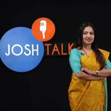 Dipali A. Chandak, in a yellow saree with her arms folded, standing in front of the Josh Talk logo